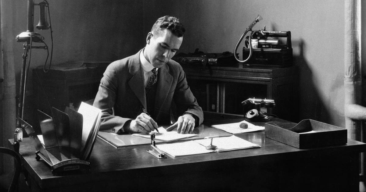 A black and white photo of Henry J.E. Reid, Directory of the Langley Aeronautics Laborator, in a suit writing while sitting at a desk. 