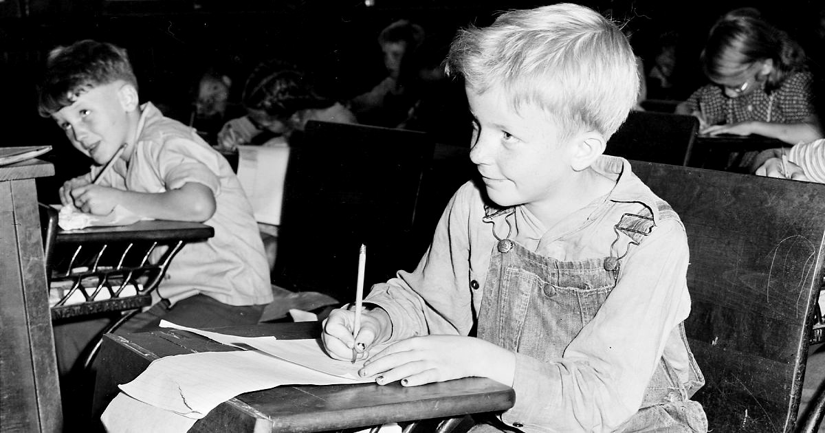 Black and white photo of a young boy at a school desk. 