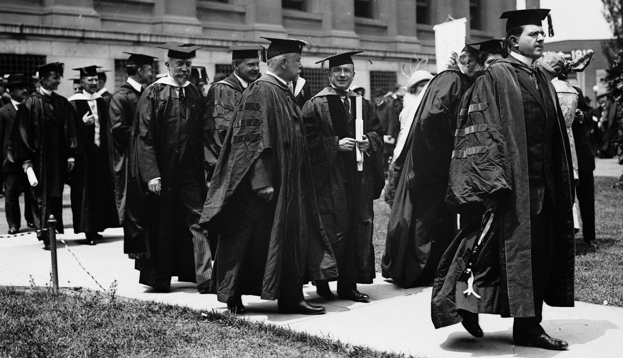 A black and white photo from the 1913 Columbia University Commencement featuring a group of men in doctoral gowns wearing mortarboards. Nobel Prize winner Alexis Carrel is amongst them. 