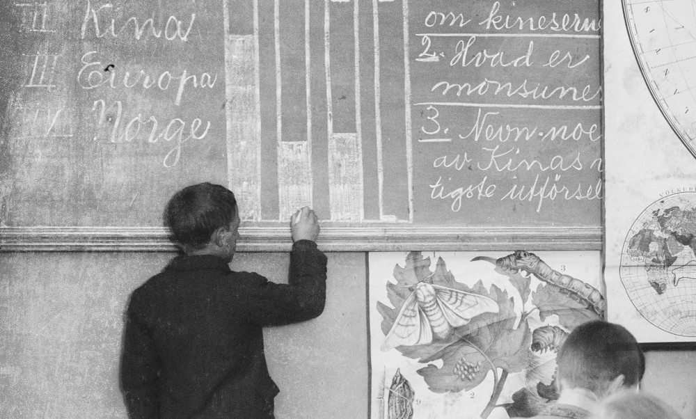 A black and white photograph of a child filling in a bar graph on a chalkboard. 