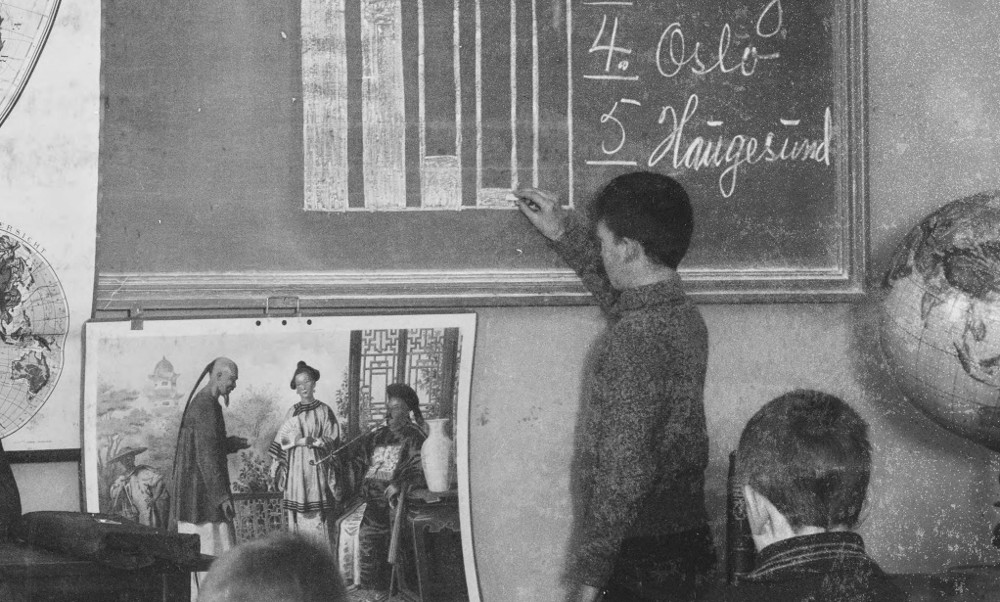 A black and white photograph of a child filling in a bar graph on a chalkboard. 