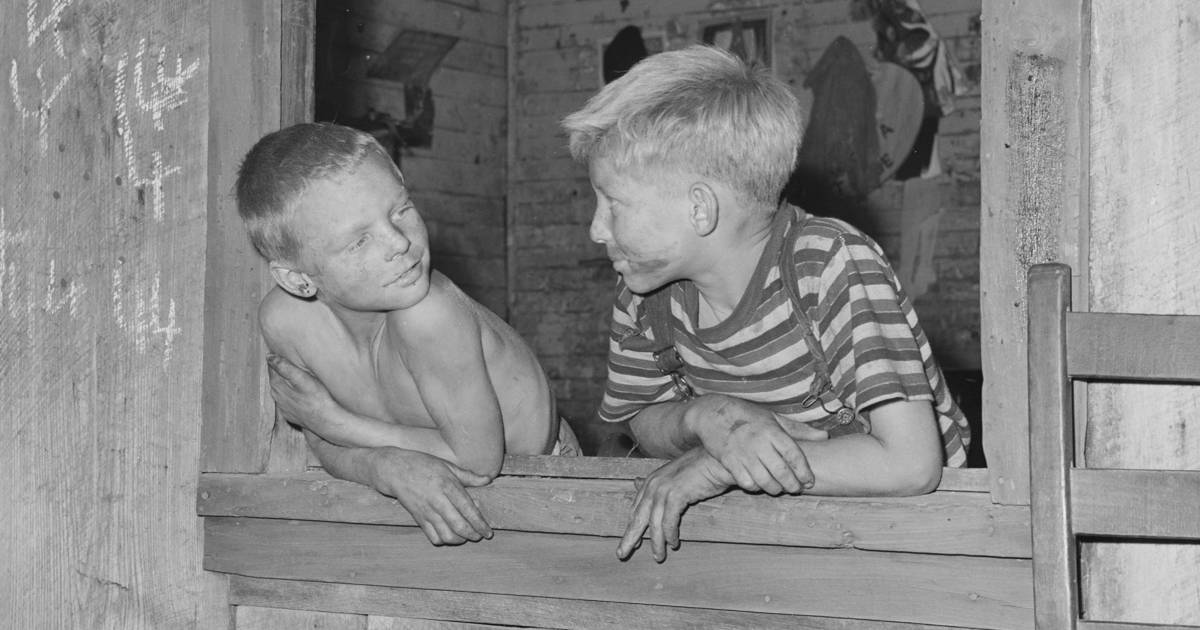 Black and white photo of two young boys hanging out a window, their faces smudged with soot. 