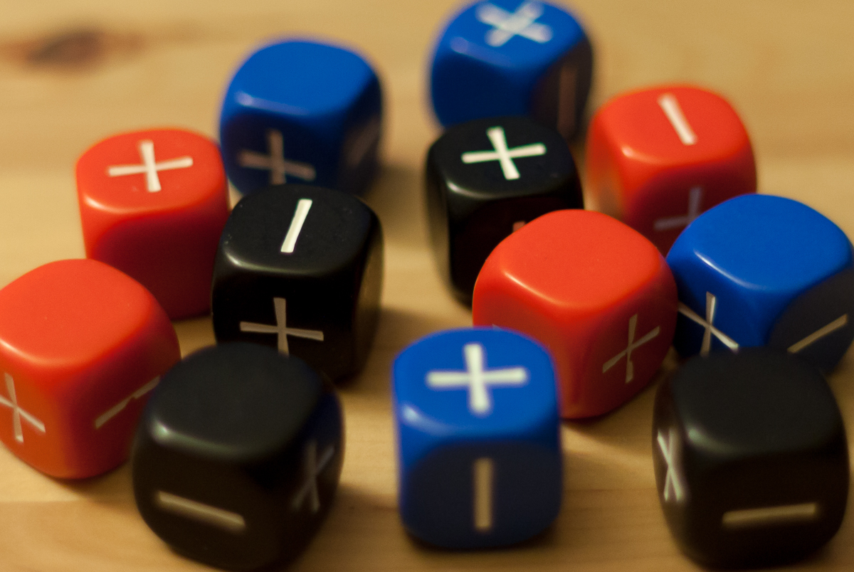 Three sets of four Fate dice, colored blue, red, and black, resting on top of a wooden table.