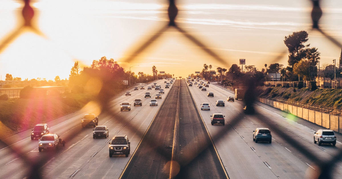 View of a freeway seen through a chain-link fence at sunset.