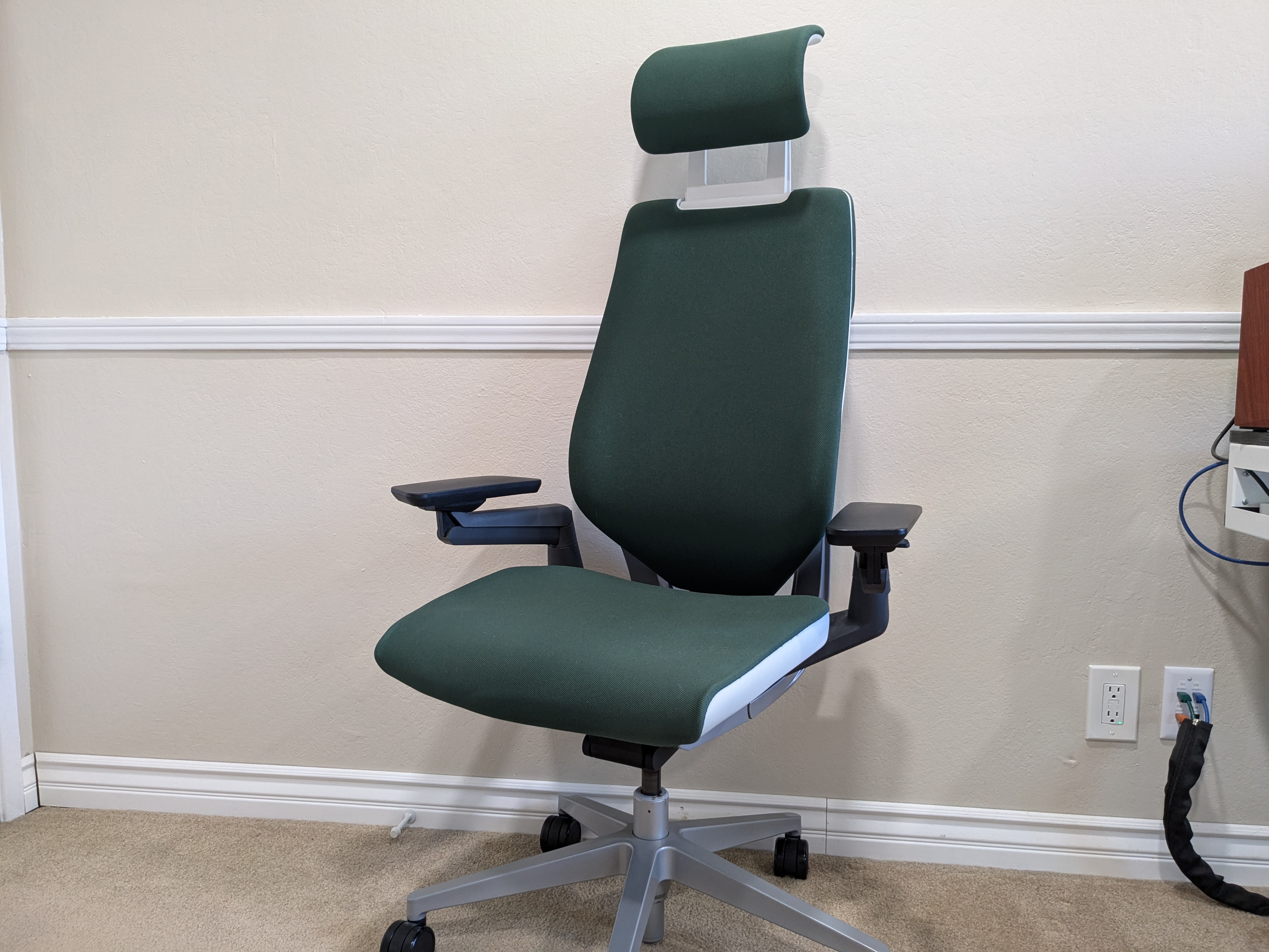 The Steelcase Gesture in my office against a wall. The chair has green upholstry and a headrest. The arms are black. The base is silver-grey. 