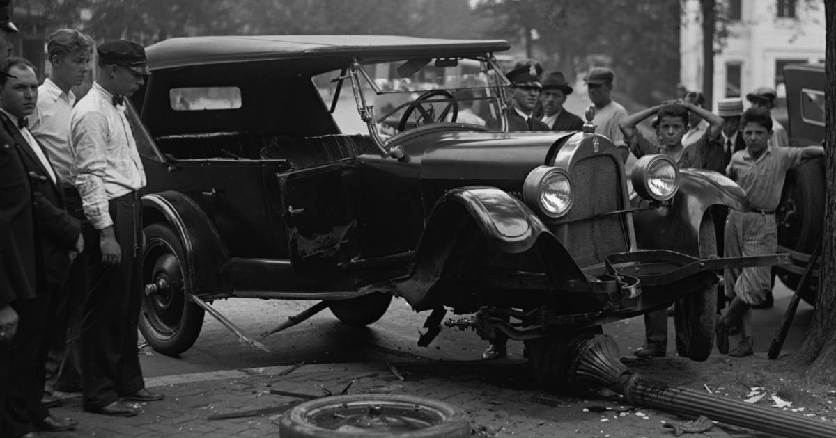 Black and white photo from 1926 of men and boys crowded around a car that has driven into a lamppost and lost it's front left wheel.