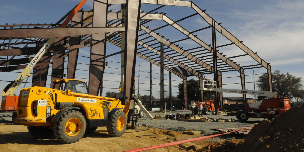 A construction site with the metal frame of a building and various pieces of heavy equipment parked around it. 